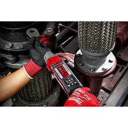 A person wearing red gloves uses an M12 FUEL 1/2” Digital Torque Wrench with ONE-KEY App Shot to tighten a bolt in an industrial setting.