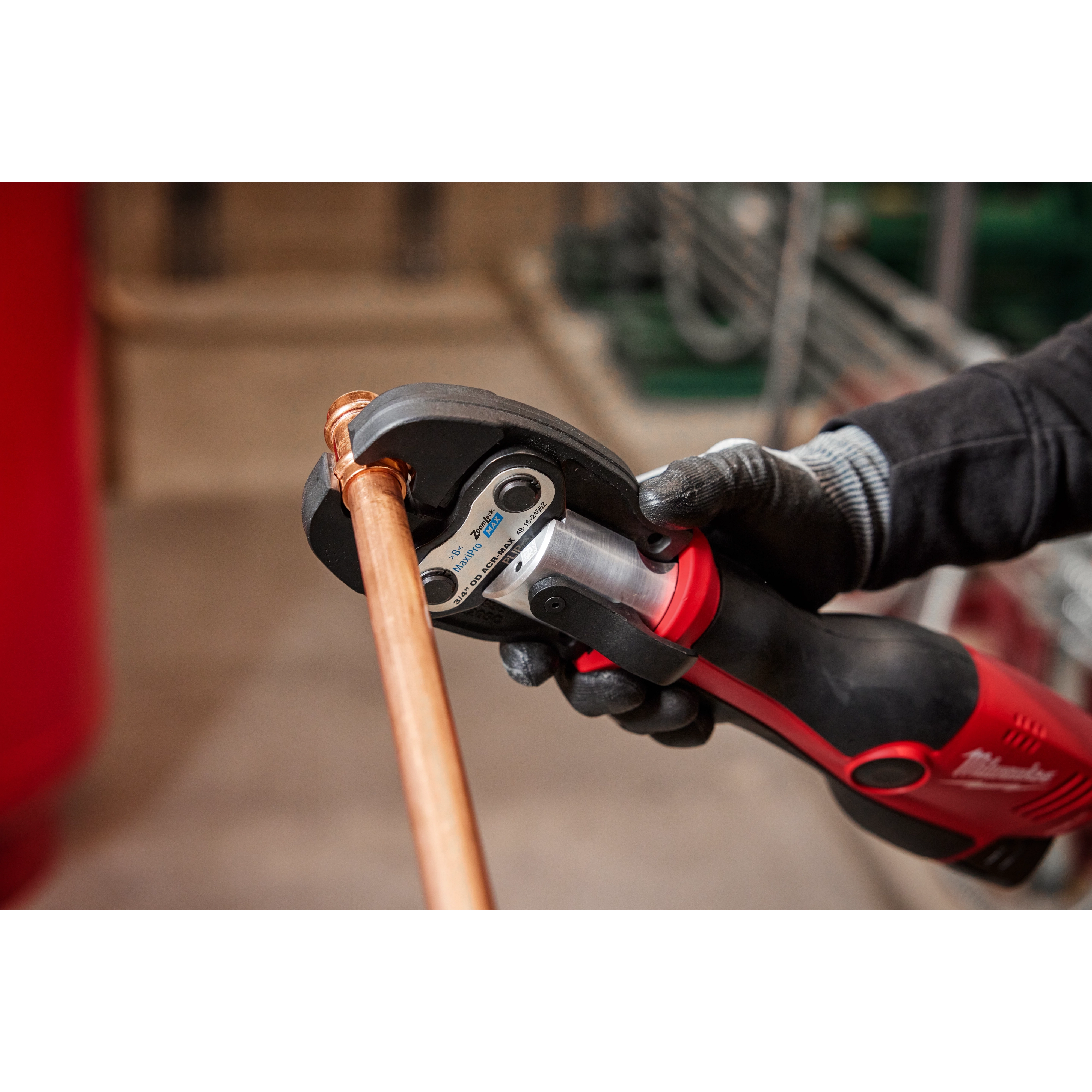A person using the 1-1/8" ZoomLock MAX Press Jaw for M12 FORCE LOGIC Press Tools to connect a copper pipe in a workshop.