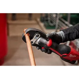 A person using the 1-1/8" ZoomLock MAX Press Jaw for M12 FORCE LOGIC Press Tools to connect a copper pipe in a workshop.