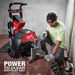 A worker operates the MX FUEL Sewer Drum Machine with POWERTREDZ. The machine is black and red, with wheels for portability.