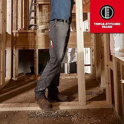 A man wearing Work Pants stands at a construction site. The pants are gray with several pockets, a tool hanging from one, and feature triple-stitched seams. The image emphasizes the durability and functionality of the Work Pants.