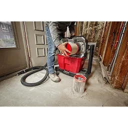 A person changes the HEPA filter of a wet/dry vacuum in a construction setting, with another filter on the floor.