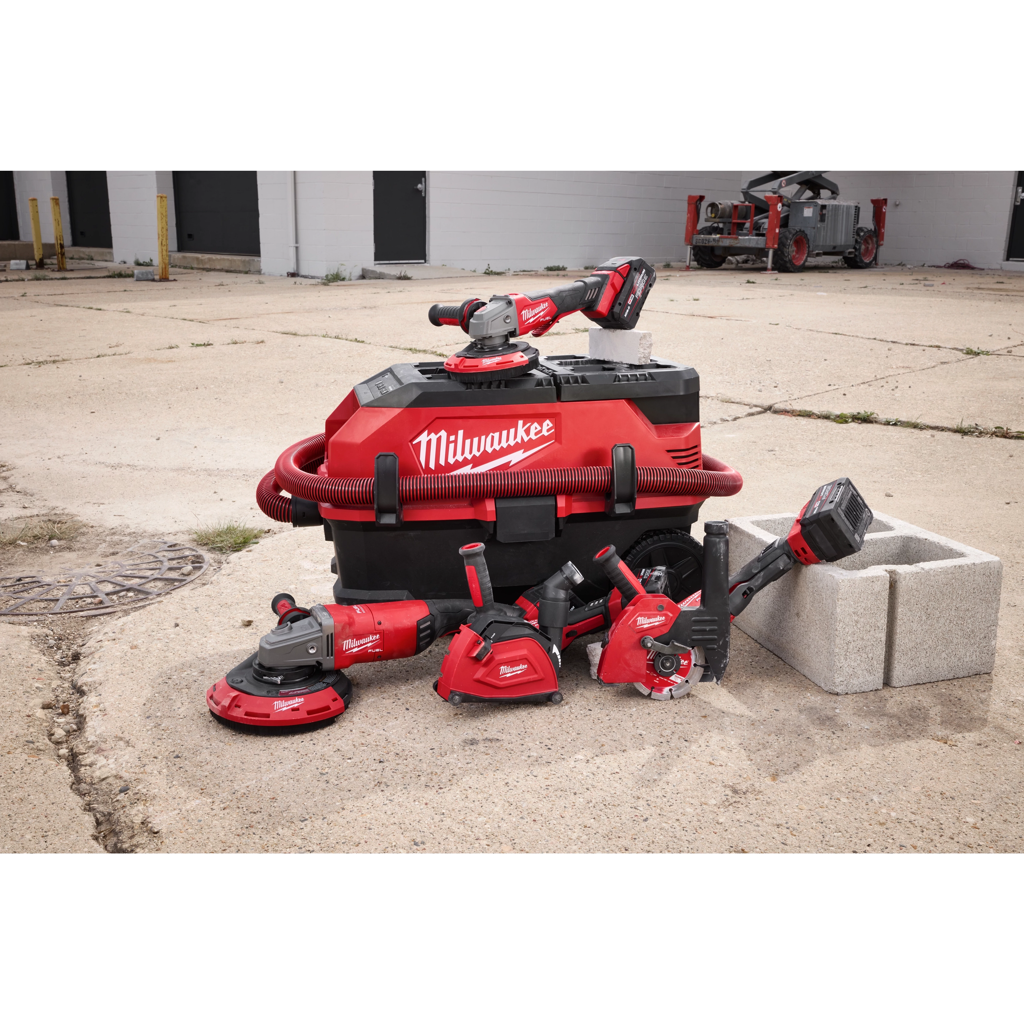 Milwaukee power tools are organized around a red and black vacuum system, branded with the word Milwaukee. The tools include grinders, drills, and saws, part of the DUST SHROUD FAMILY.
