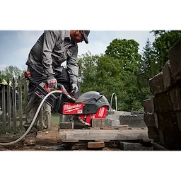 A person is using a Milwaukee saw fitted with a 14-inch DIAMOND ULTRA™ Segmented Turbo, General Purpose Diamond Blade to cut concrete blocks outdoors. The saw and blade are part of Milwaukee's MX FUEL equipment, visible against a background of trees and construction materials.