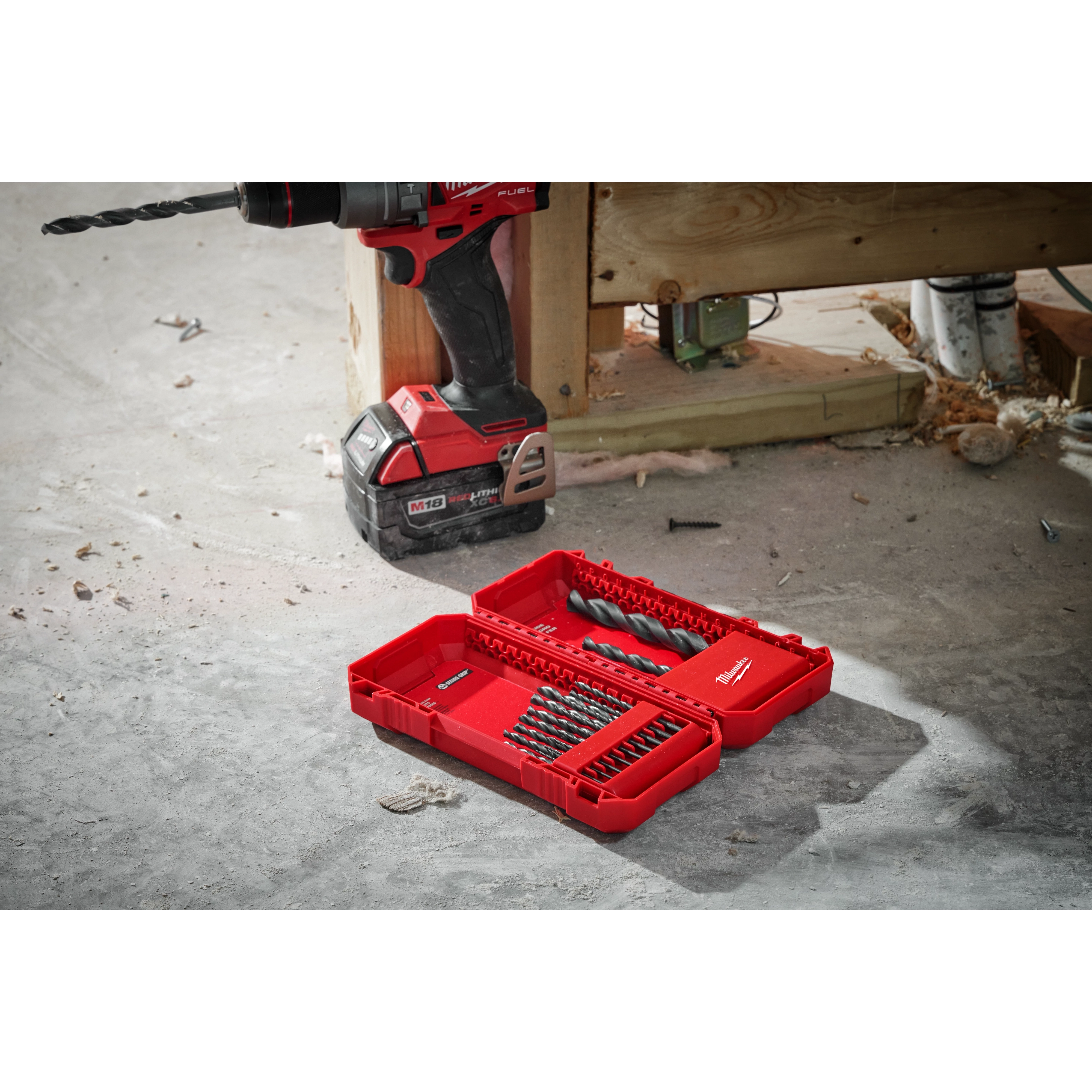 THUNDERBOLT® Black Oxide Drill Bit Set - 21PC displayed in an open red case on a workshop floor. A drill with a bit attached is positioned next to the case. The set includes various sizes of drill bits organized in rows inside the red plastic case.