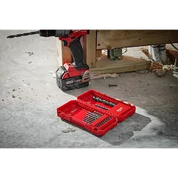 THUNDERBOLT® Black Oxide Drill Bit Set - 21PC displayed in an open red case on a workshop floor. A drill with a bit attached is positioned next to the case. The set includes various sizes of drill bits organized in rows inside the red plastic case.