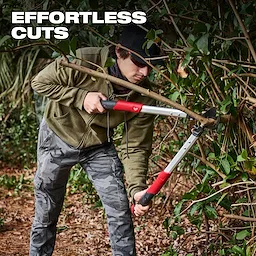 A person is using a 2" Lopper to trim a thick branch from a bush in a garden. The tool has red and black handles, and the image includes the text "EFFORTLESS CUTS" in bold white letters at the top left corner.