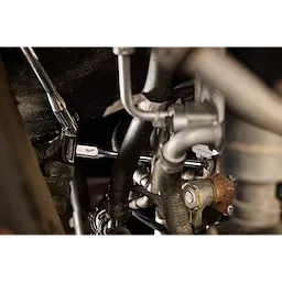 Person uses a 3/8" Drive 6mm Long Ball End Hex Bit Socket to work on machinery with various metal pipes and bolts. The socket appears engaged with a ratchet handle, performing maintenance or assembly tasks.