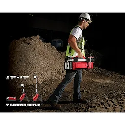 Construction worker carrying the M18 ROCKET Dual Pack Tower Light with ONE-KEY on a rugged construction site. Setup time: 7 seconds.