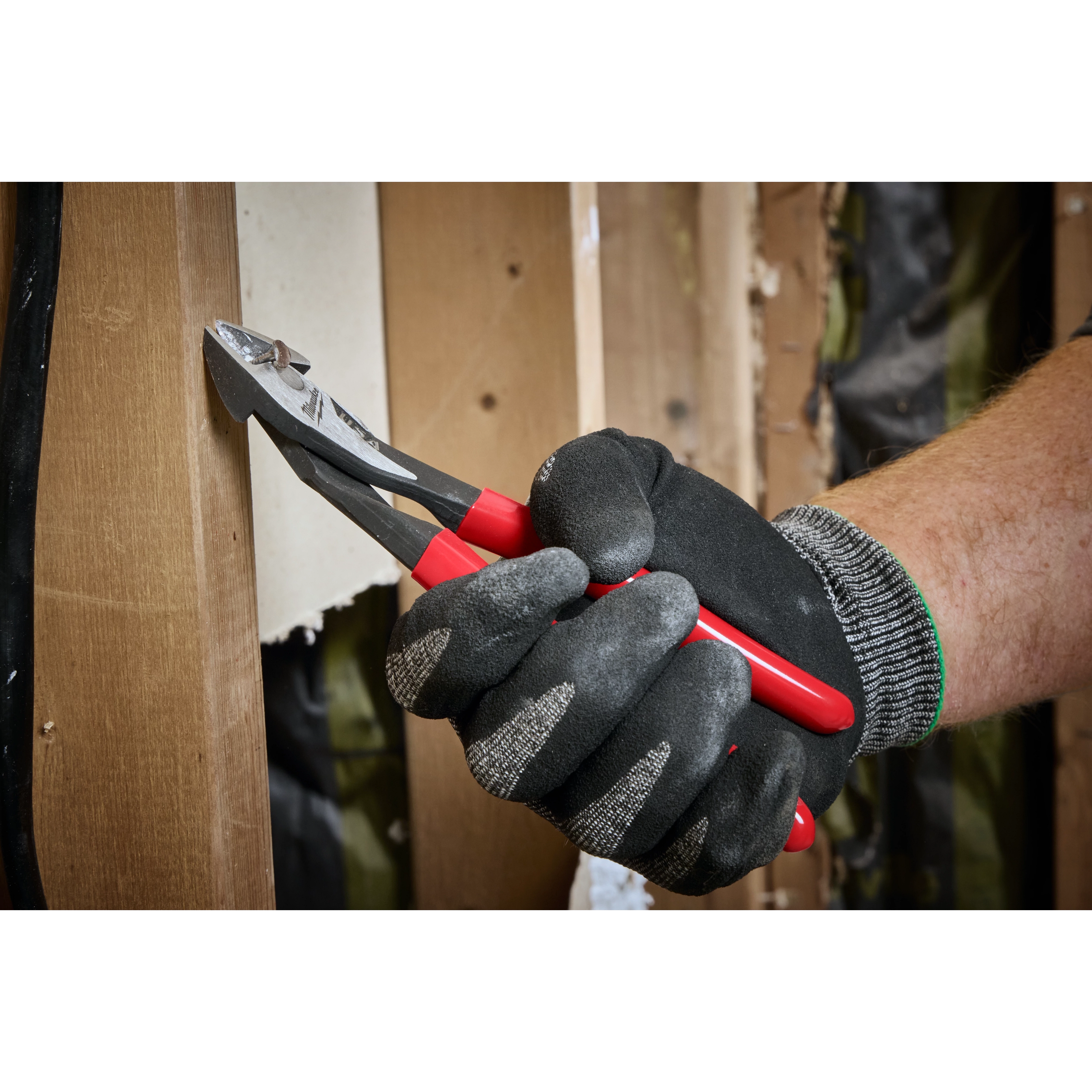 A hand wearing dark gloves uses the Knipex Diagonal Cutter to cut an object. The Knipex Diagonal Cutter has red and black handles and is designed for cutting wires and other materials.
