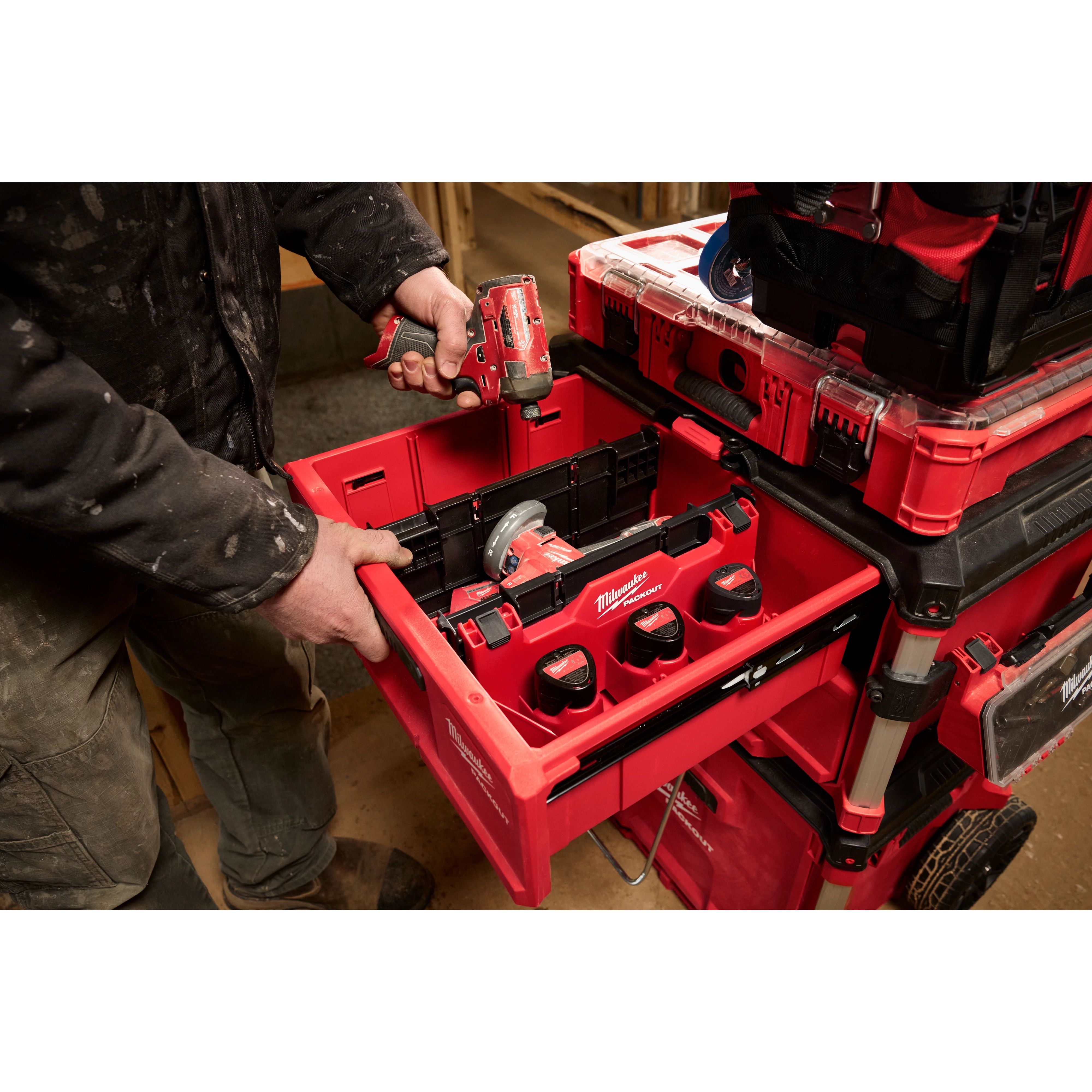 A person using a Divider for PACKOUT Drawer Tool Boxes to organize a red tool drawer with power tools and batteries.