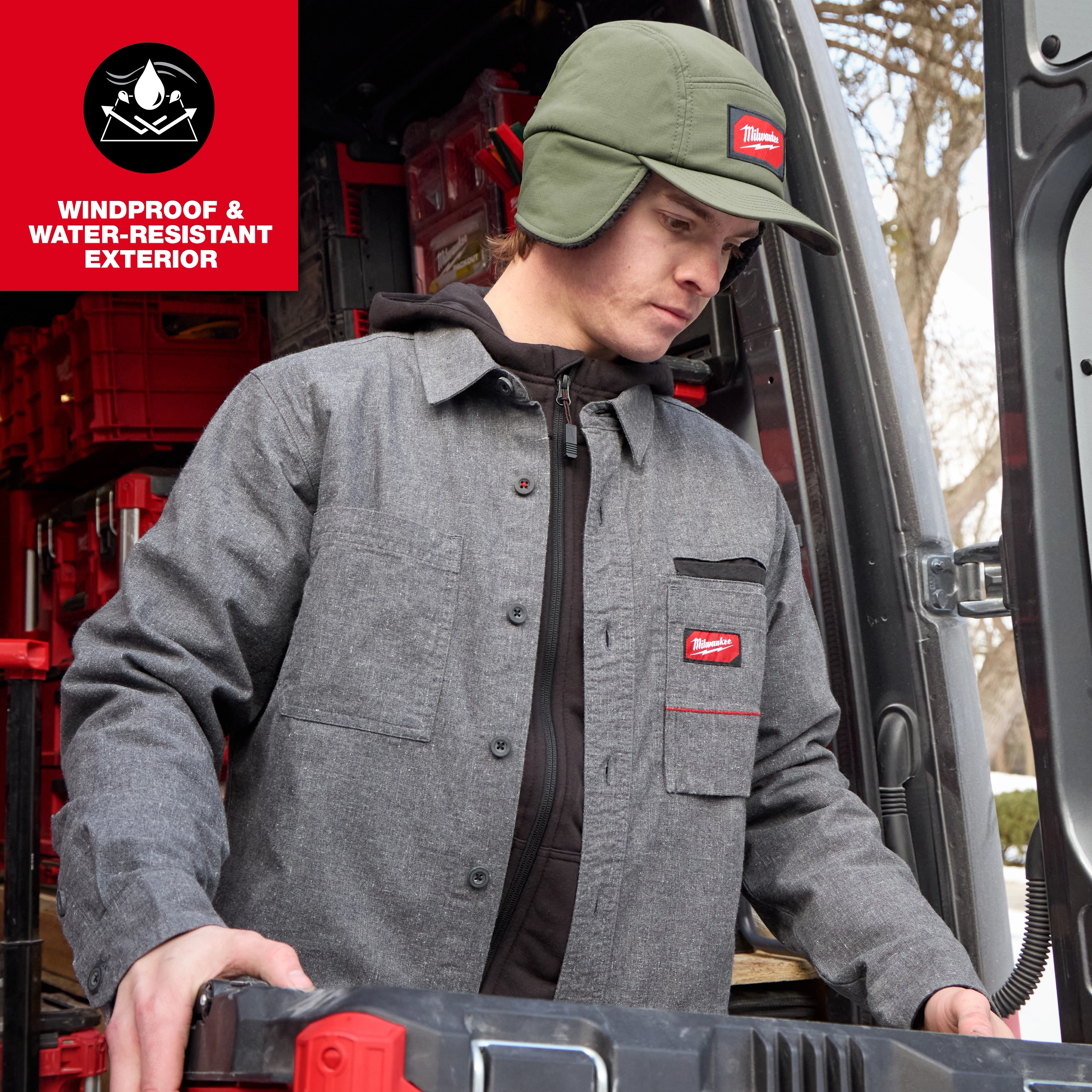 Person wearing a Milwaukee Sherpa-Lined Hat and work jacket while loading gear into a vehicle.