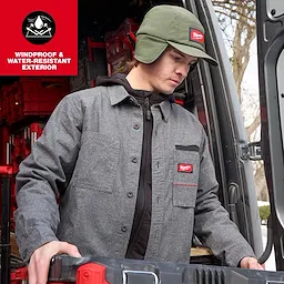 Person wearing a Milwaukee Sherpa-Lined Hat and work jacket while loading gear into a vehicle.