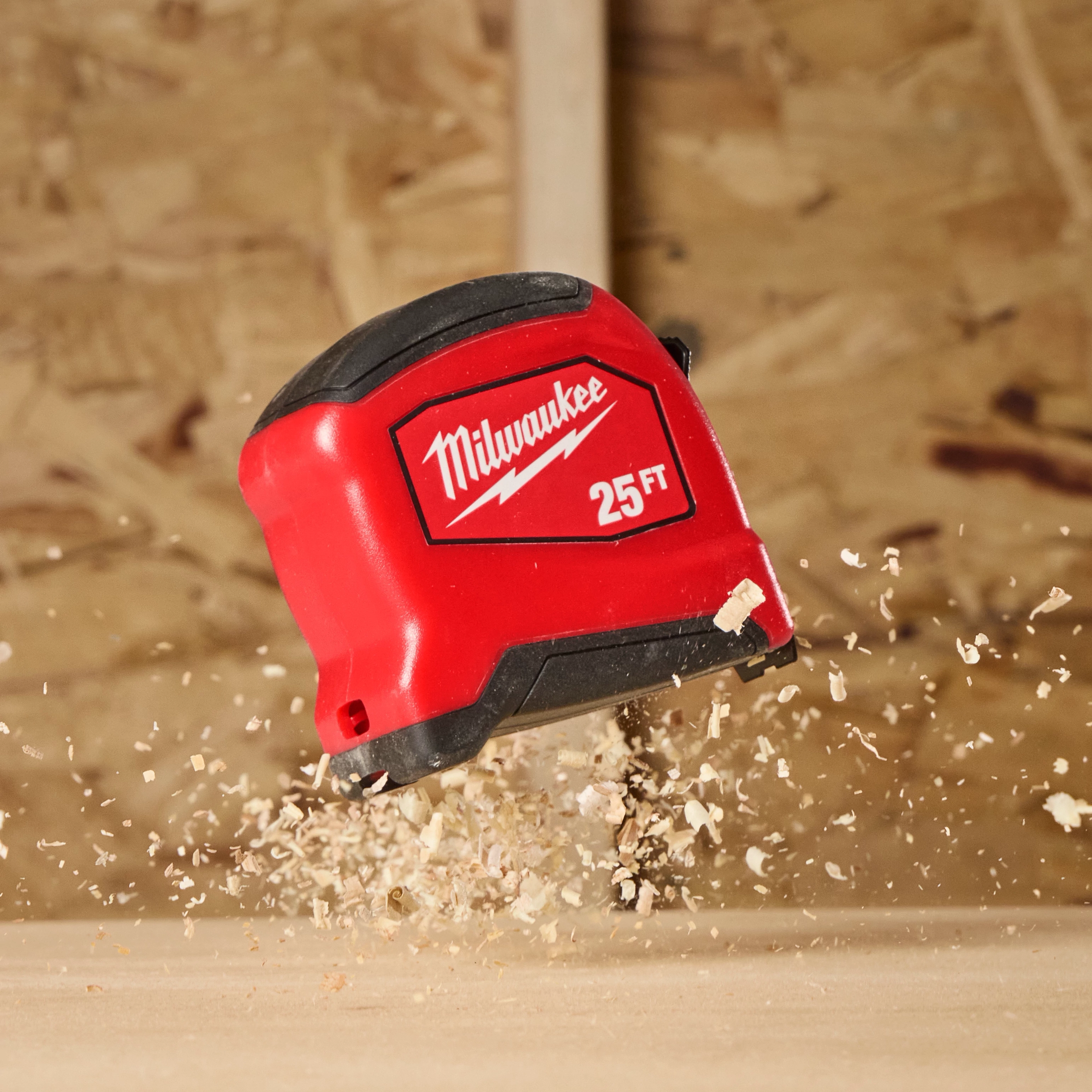 25ft Tape Measure in mid-air above a wooden surface with wood shavings flying around.