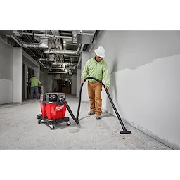 Worker using the Milwaukee M18 Fuel 9 Gallon Dual-Battery Wet/Dry Vacuum to clean a construction site interior.