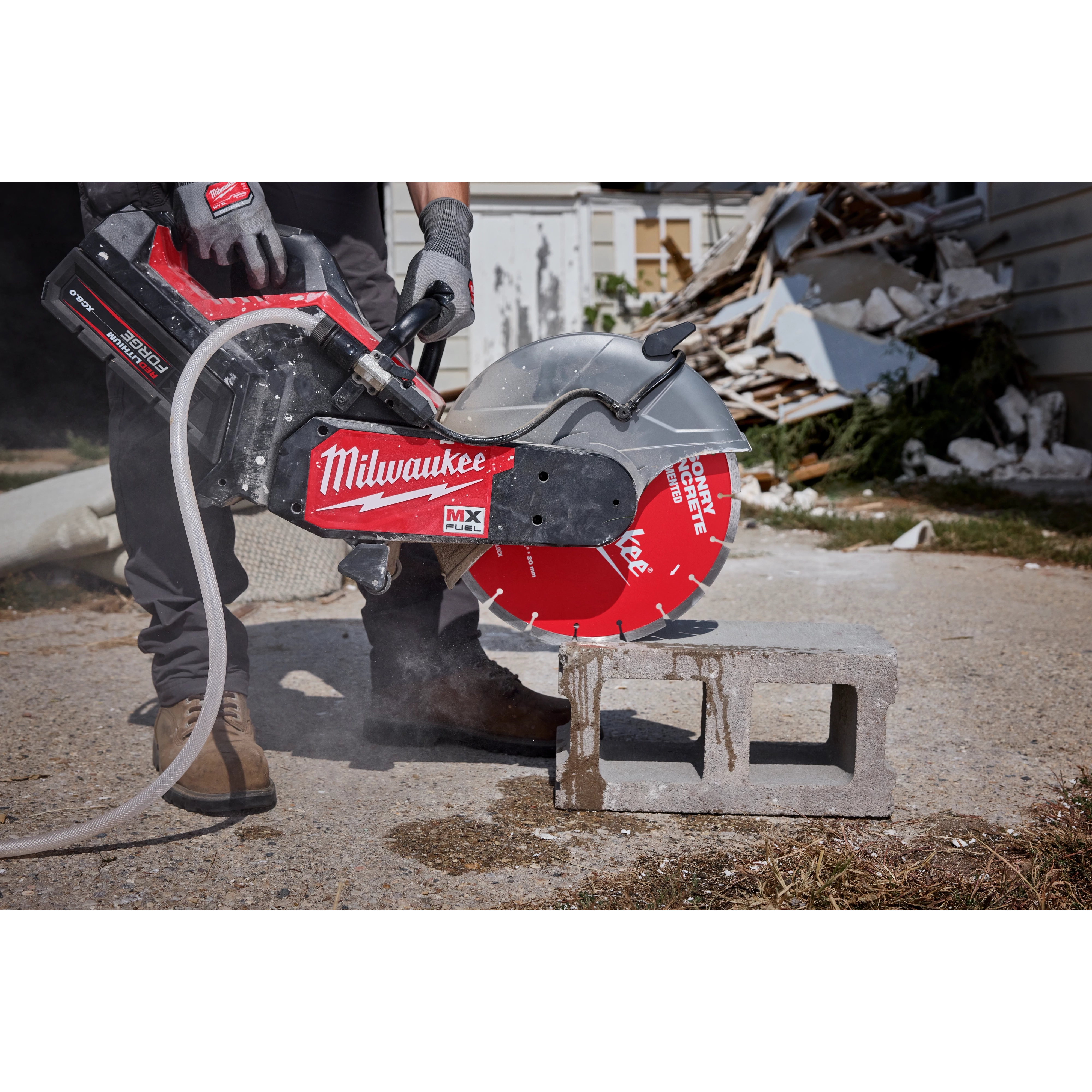 A person uses a concrete saw equipped with a red 14" Segmented Masonry & Concrete Diamond Blade to cut a concrete block. Debris is scattered in the background, and the saw emits dust during the cutting process. The "Milwaukee" brand label is visible on the saw.