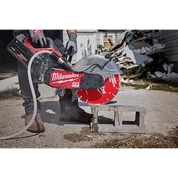 A person uses a concrete saw equipped with a red 14" Segmented Masonry & Concrete Diamond Blade to cut a concrete block. Debris is scattered in the background, and the saw emits dust during the cutting process. The "Milwaukee" brand label is visible on the saw.