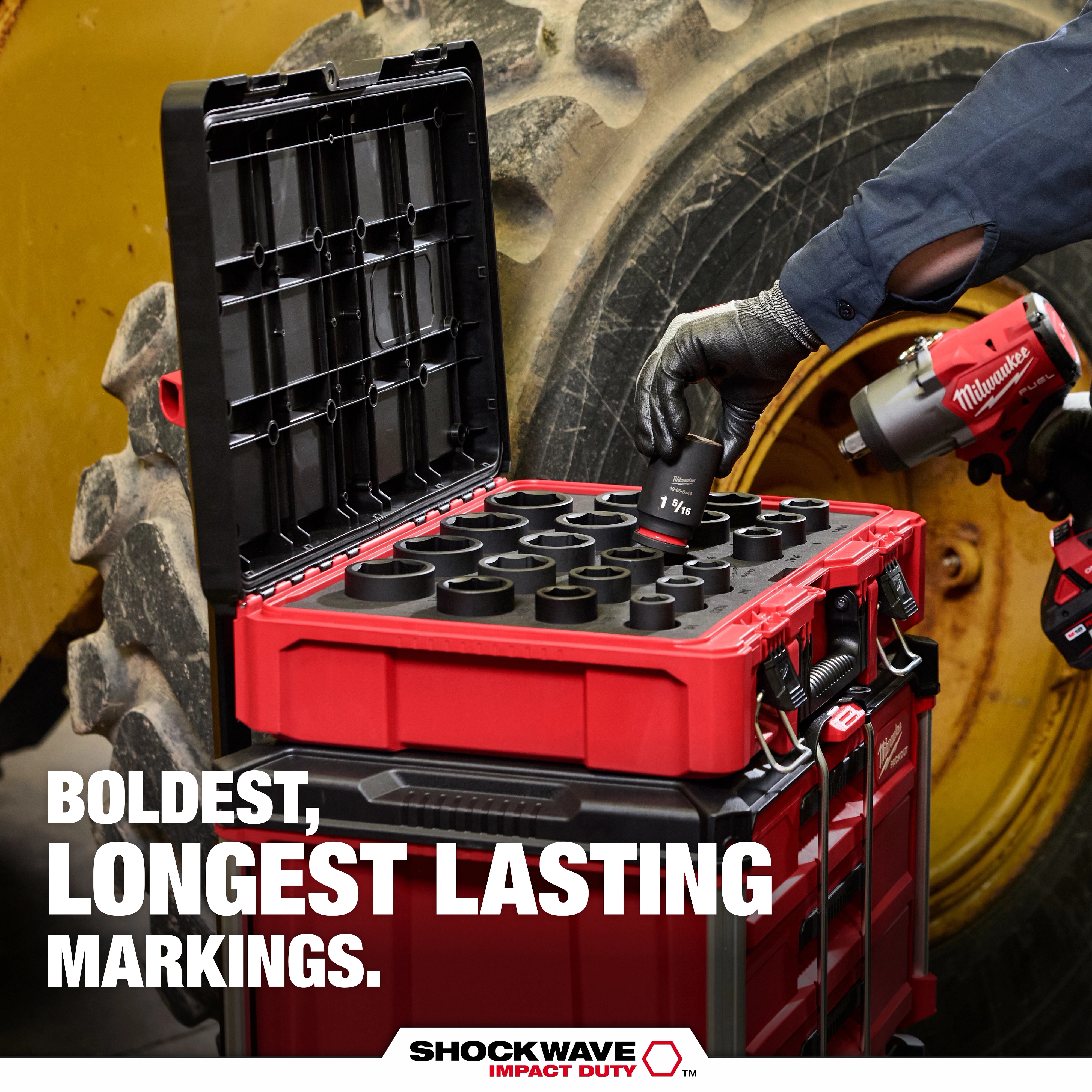 Open red PACKOUT case holding SHOCKWAVE Impact Duty sockets beside large machinery tire.