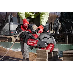 A person wearing a green jacket and red gloves uses a Milwaukee power saw with a 14" DIAMOND ULTRA™ Segmented Turbo, General Purpose Diamond Blade to cut concrete blocks on a construction site.