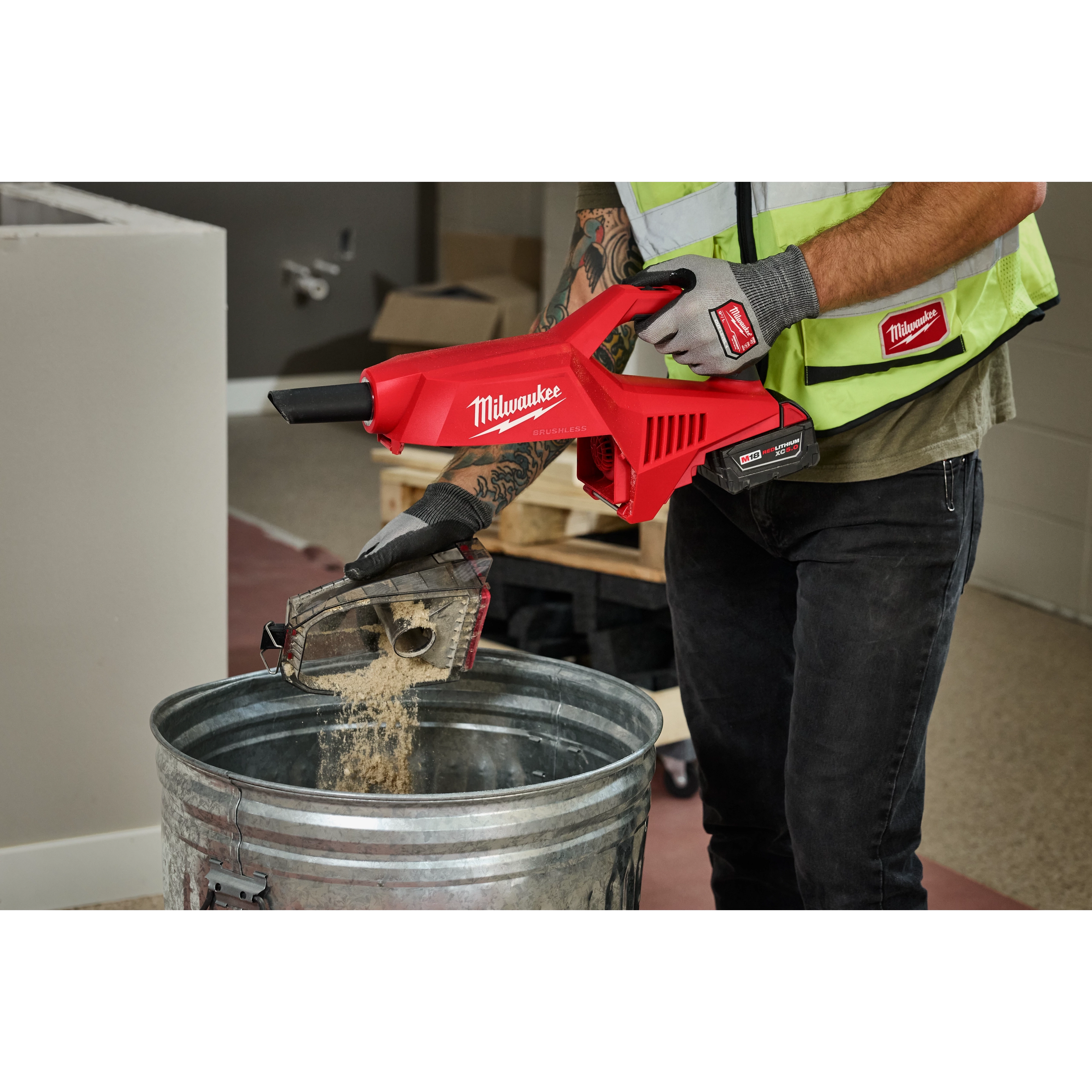 A person is emptying dust from the M18 Brushless Handheld Vacuum into a metal trash can.