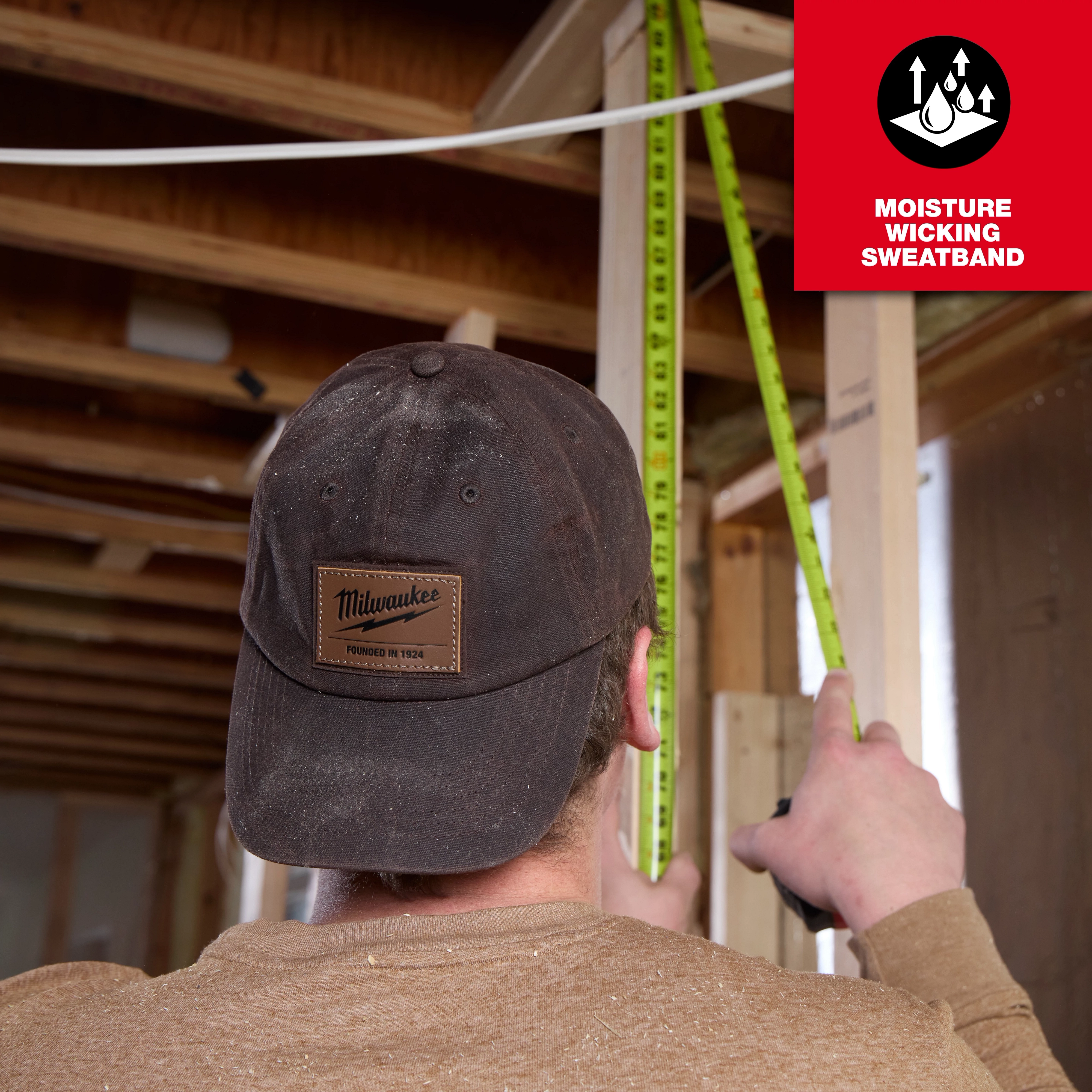 Person measuring in a construction site, wearing a Waxed Canvas Adjustable Hat. Inset text highlights the moisture-wicking sweatband feature.