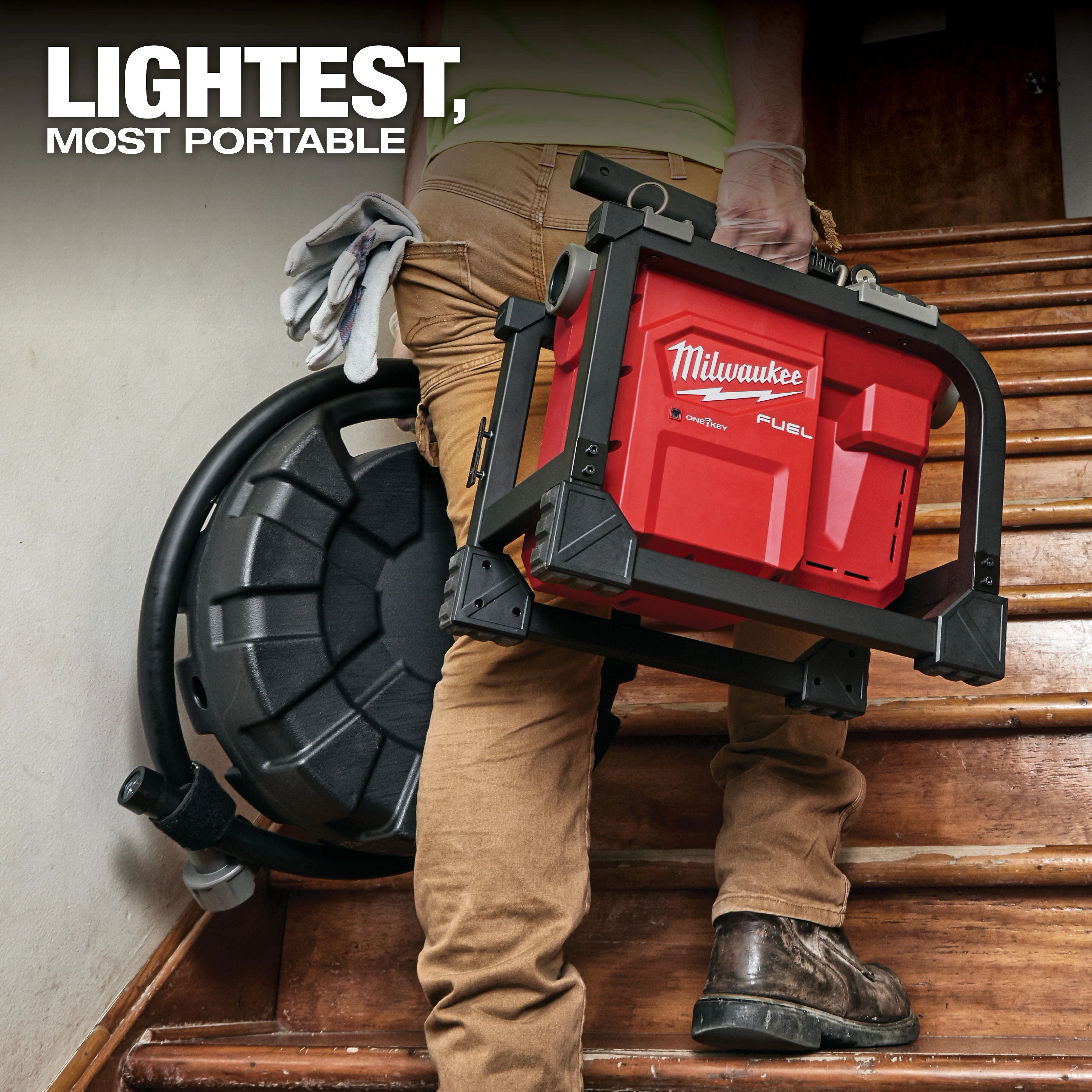 A person carries a Milwaukee Fuel portable air compressor up a wooden staircase. The product slogan "Lightest, Most Portable" appears in bold text at the top left of the image. The compressor is red with black casing and features ergonomic handles for easy transport.