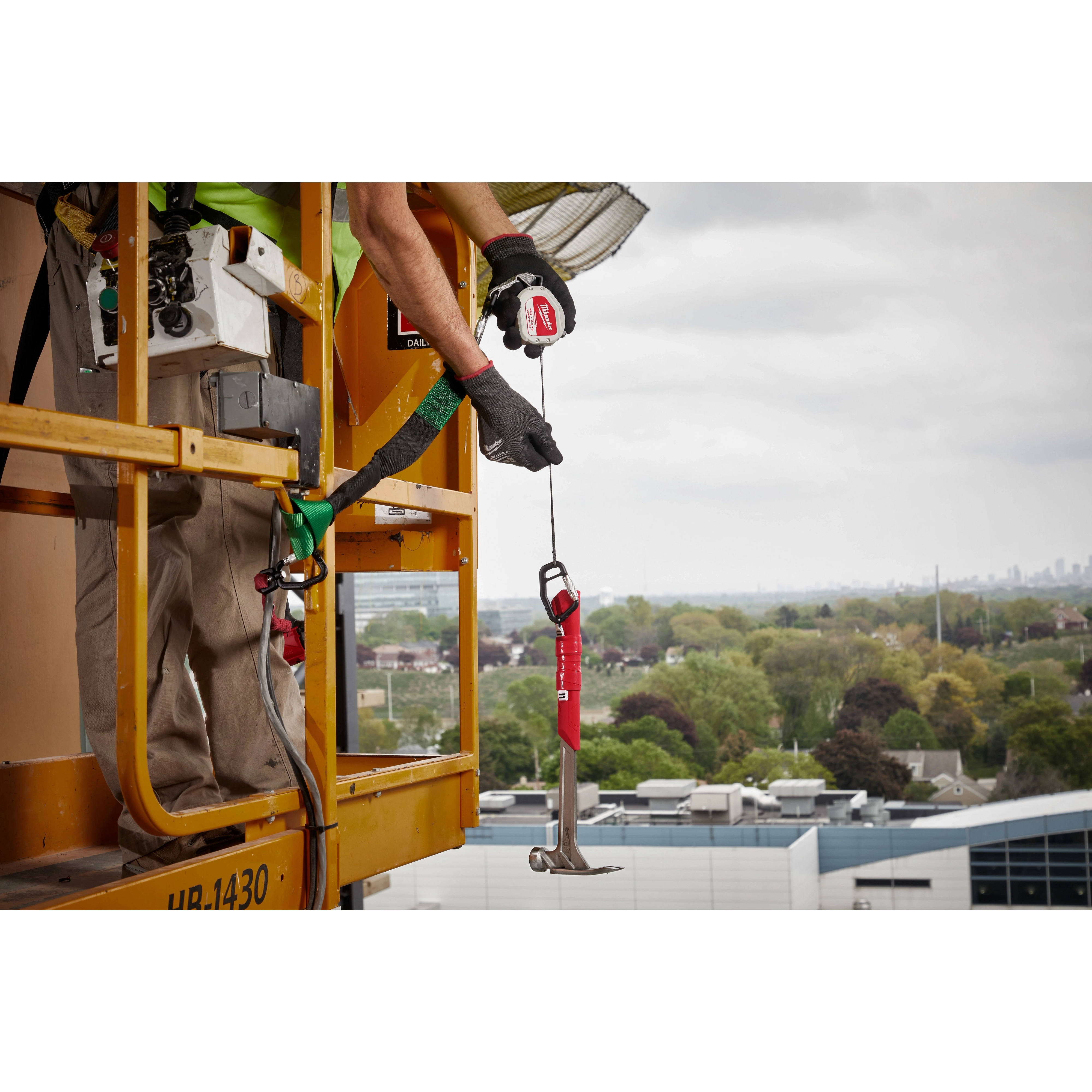A worker uses the 5LB Quick-Connect Retractable Tool Lanyard to secure a heavy-duty wrench while standing on an elevated platform. The tool lanyard prevents tools from falling, enhancing safety. The background shows an urban landscape with buildings and greenery.