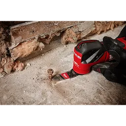 The NITRUS CARBIDE™ Extreme Metal Universal Fit OPEN-LOK™ Multi-Tool Blade is shown attached to a power tool, cutting a rusty bolt protruding from a concrete floor. The background includes exposed insulation and wooden beams.