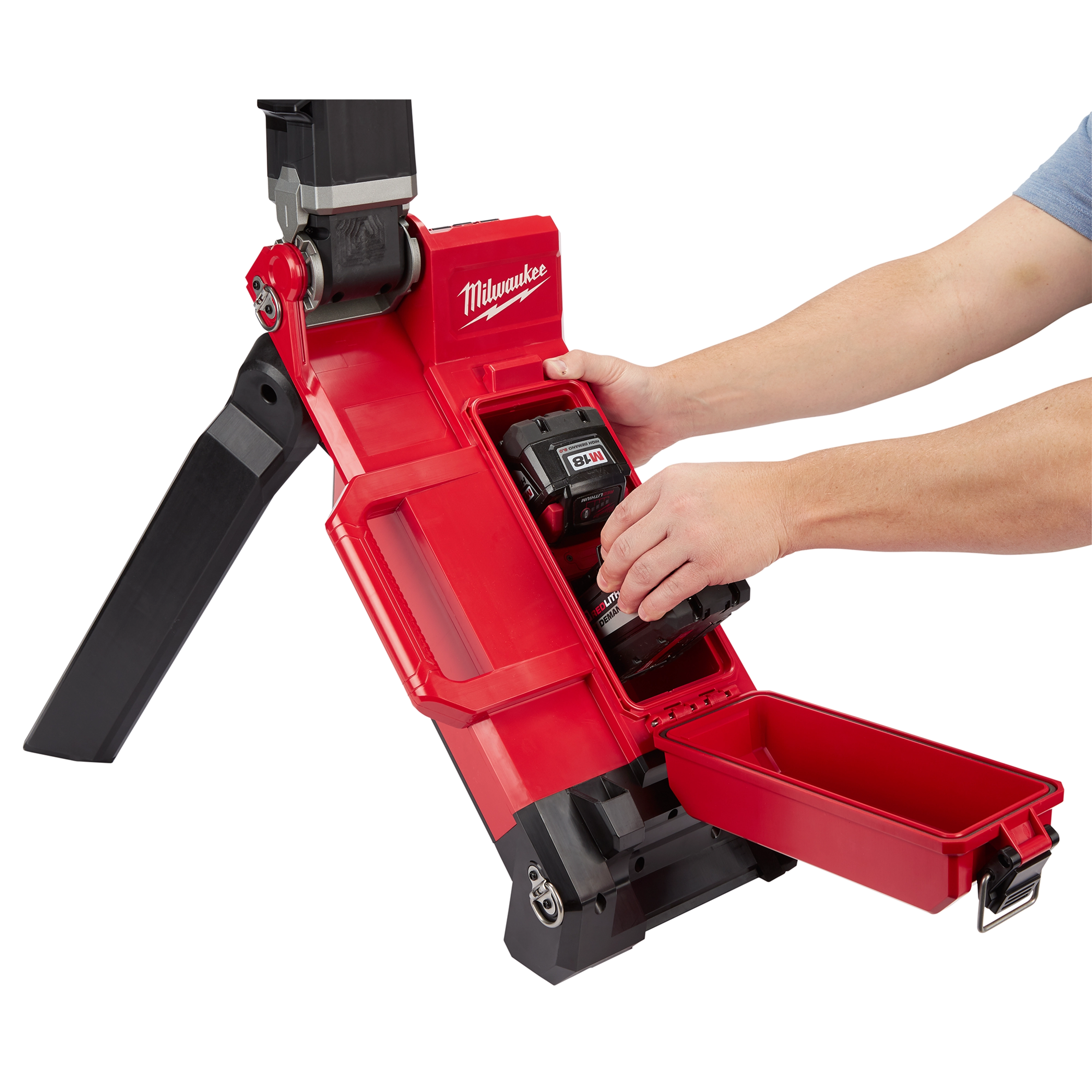 Person inserting a battery into the M18 Rocket Light, a red portable work light with foldable legs and a compartment for tools.