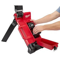 Person inserting a battery into the M18 Rocket Light, a red portable work light with foldable legs and a compartment for tools.