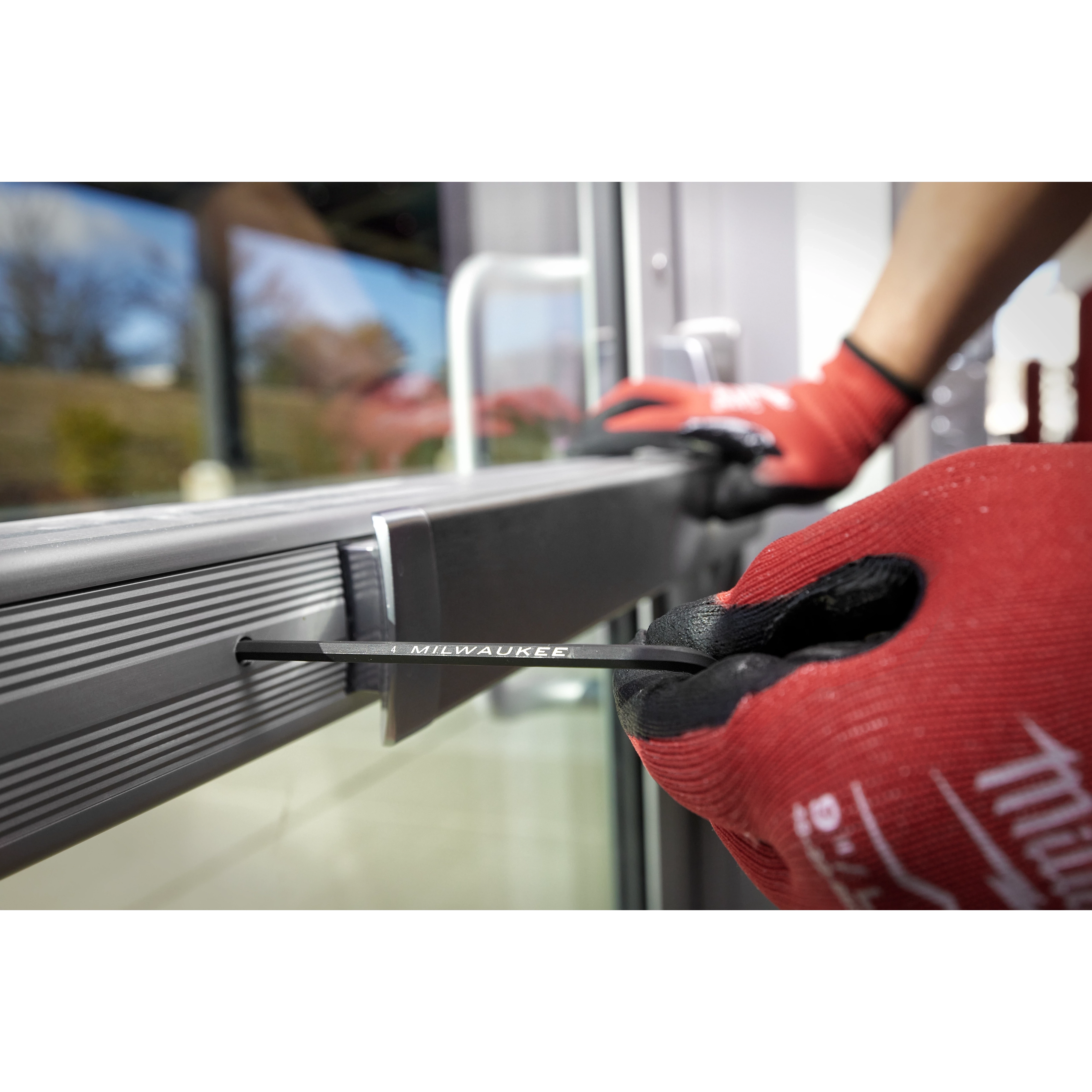 A person wearing red gloves uses a 9-Key Ball End L-Key Set - Metric to adjust a metal door frame with a hex key.