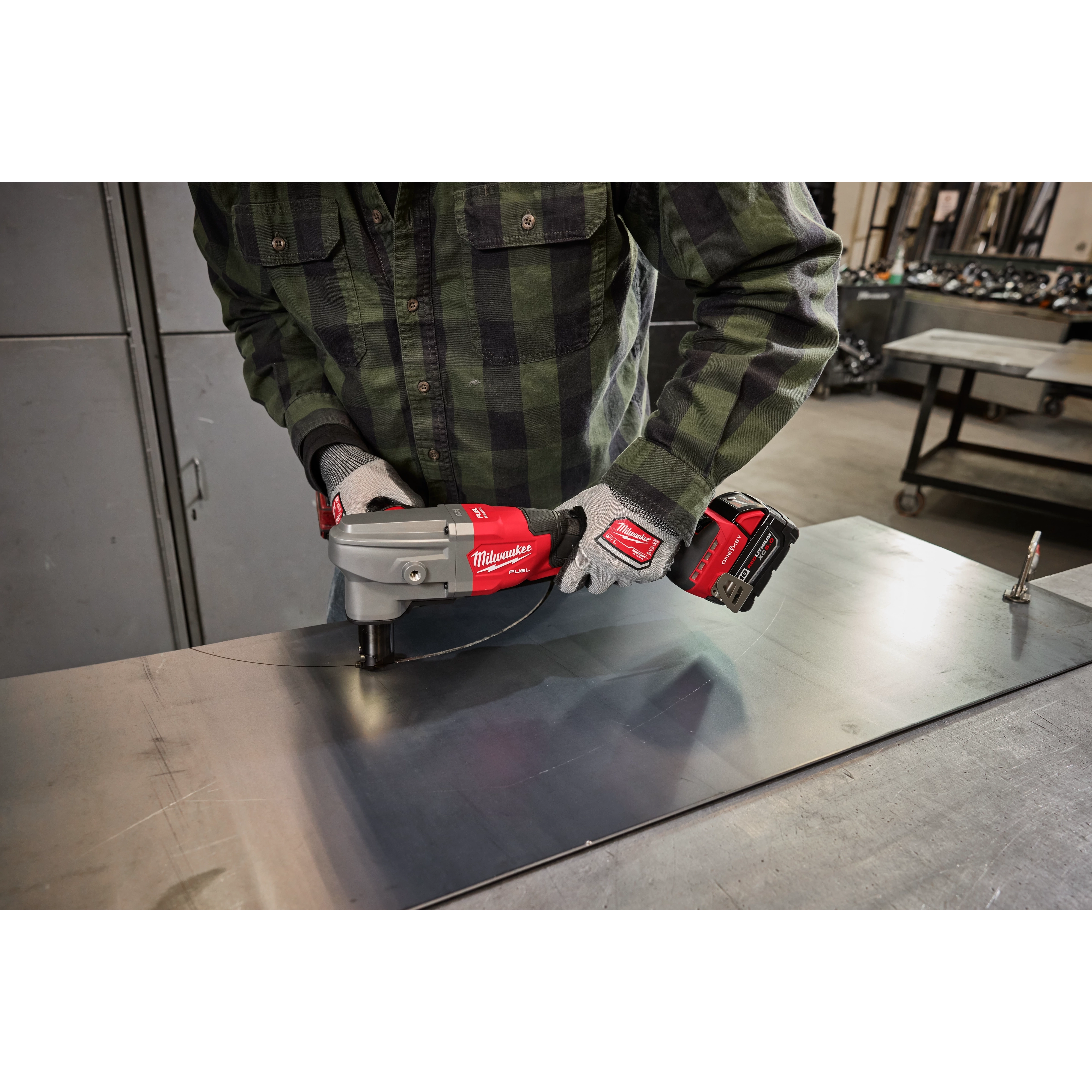 A person in a work area uses the M18 FUEL™ 10 Gauge Nibbler, with the tool making precise cuts on a metal sheet. The nibbler is red and gray, bearing the Milwaukee brand logo.