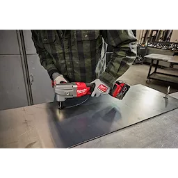 A person in a work area uses the M18 FUEL™ 10 Gauge Nibbler, with the tool making precise cuts on a metal sheet. The nibbler is red and gray, bearing the Milwaukee brand logo.