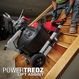 A person uses the MX FUEL Sewer Drum Machine with POWERTREDZ to lift it up a staircase, showing its mobility and lift-assist feature.