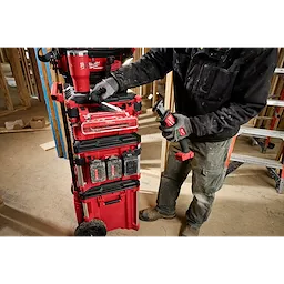 A worker adjusts a PACKOUT Tool Box Accessory Case Attachment on a red rolling tool chest at a construction site.