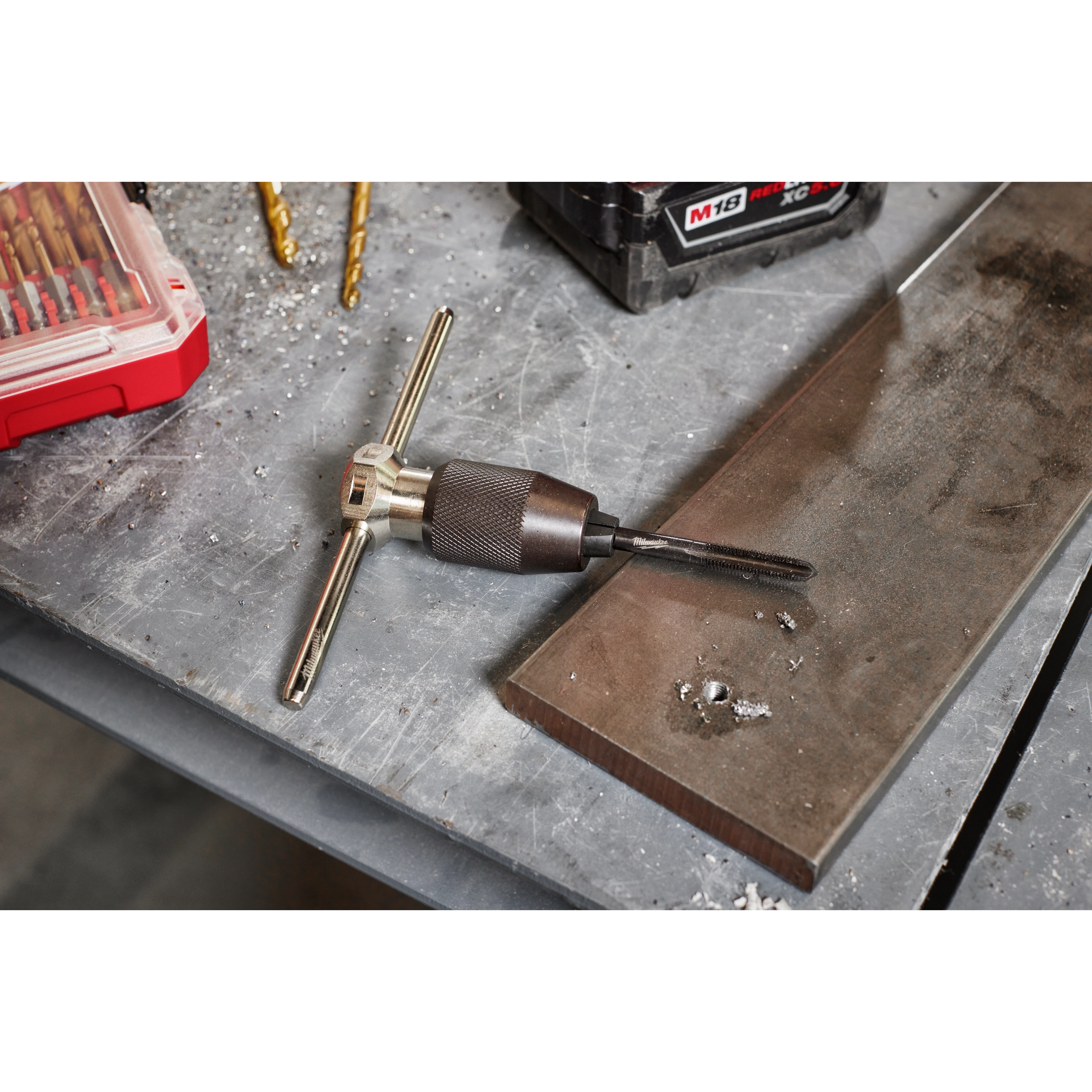 Tap Collet for Taps up to 1/2” & T Handle Bar is placed on a workbench amidst metal shavings and other tools. The T handle allows for manual control of the tap, which is used for threading holes.