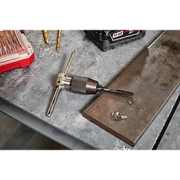 Tap Collet for Taps up to 1/2” & T Handle Bar is placed on a workbench amidst metal shavings and other tools. The T handle allows for manual control of the tap, which is used for threading holes.