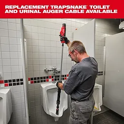 A person is using the Trapsnake toilet and urinal auger to clean a commercial urinal in a public restroom. The auger is a long tool with a red handle designed for unclogging and maintaining plumbing. Text above indicates availability of replacement cables for the Trapsnake auger.