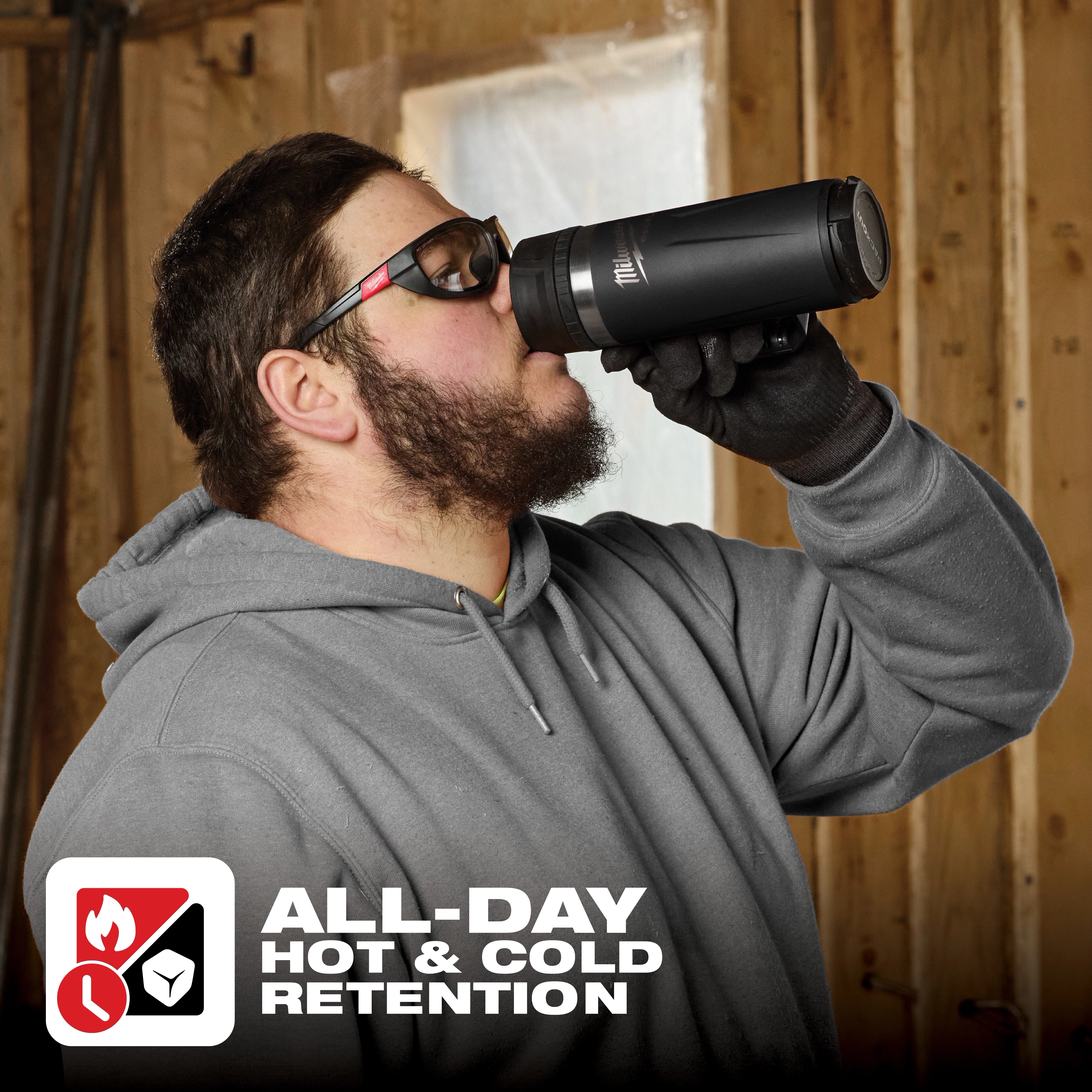 Person in a grey hoodie drinking from a PACKOUT 18oz Insulated Mug with Sip Lid in a wooden interior. Text reads "All-Day Hot & Cold Retention."