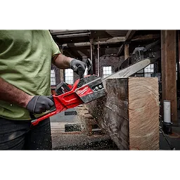 Person in a workshop using a Milwaukee chainsaw to cut a large wooden beam, with sawdust flying.