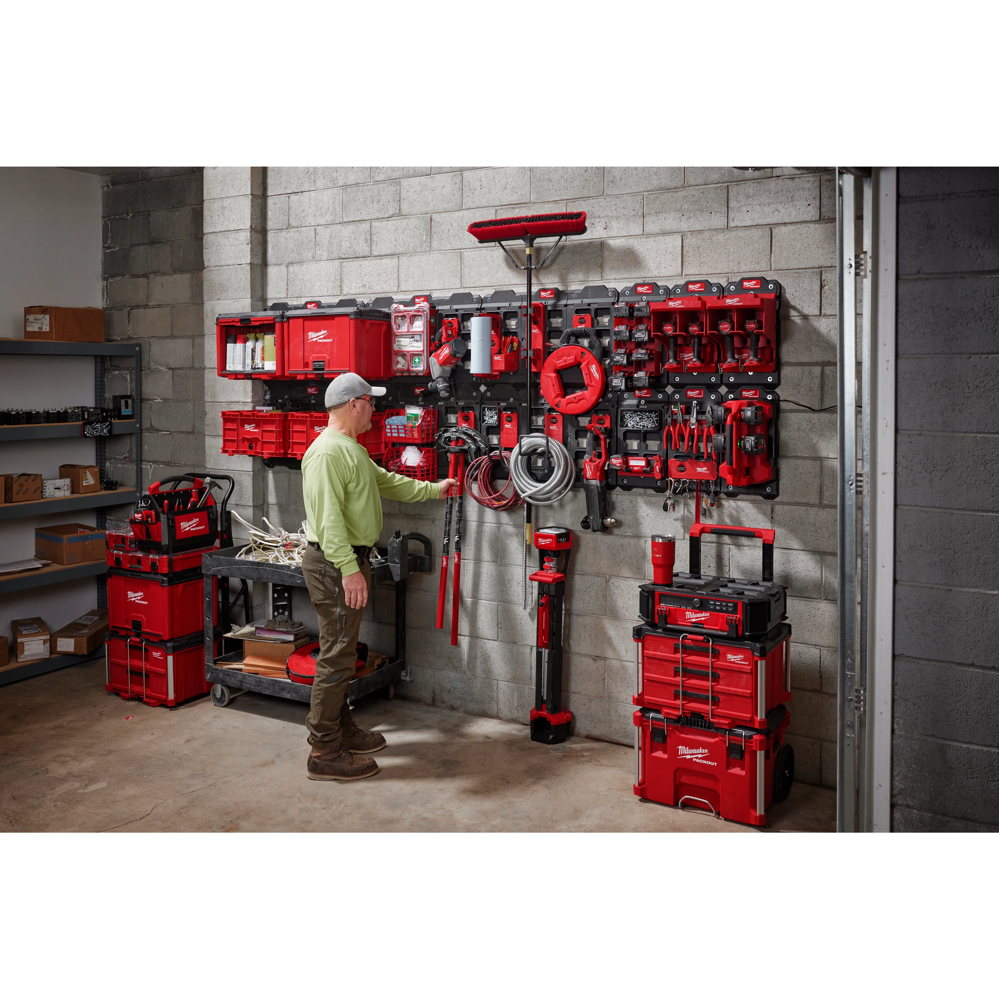 Man organizing tools in a garage using March 2023 Packout Shop Storage system with red toolboxes and wall-mounted storage units.