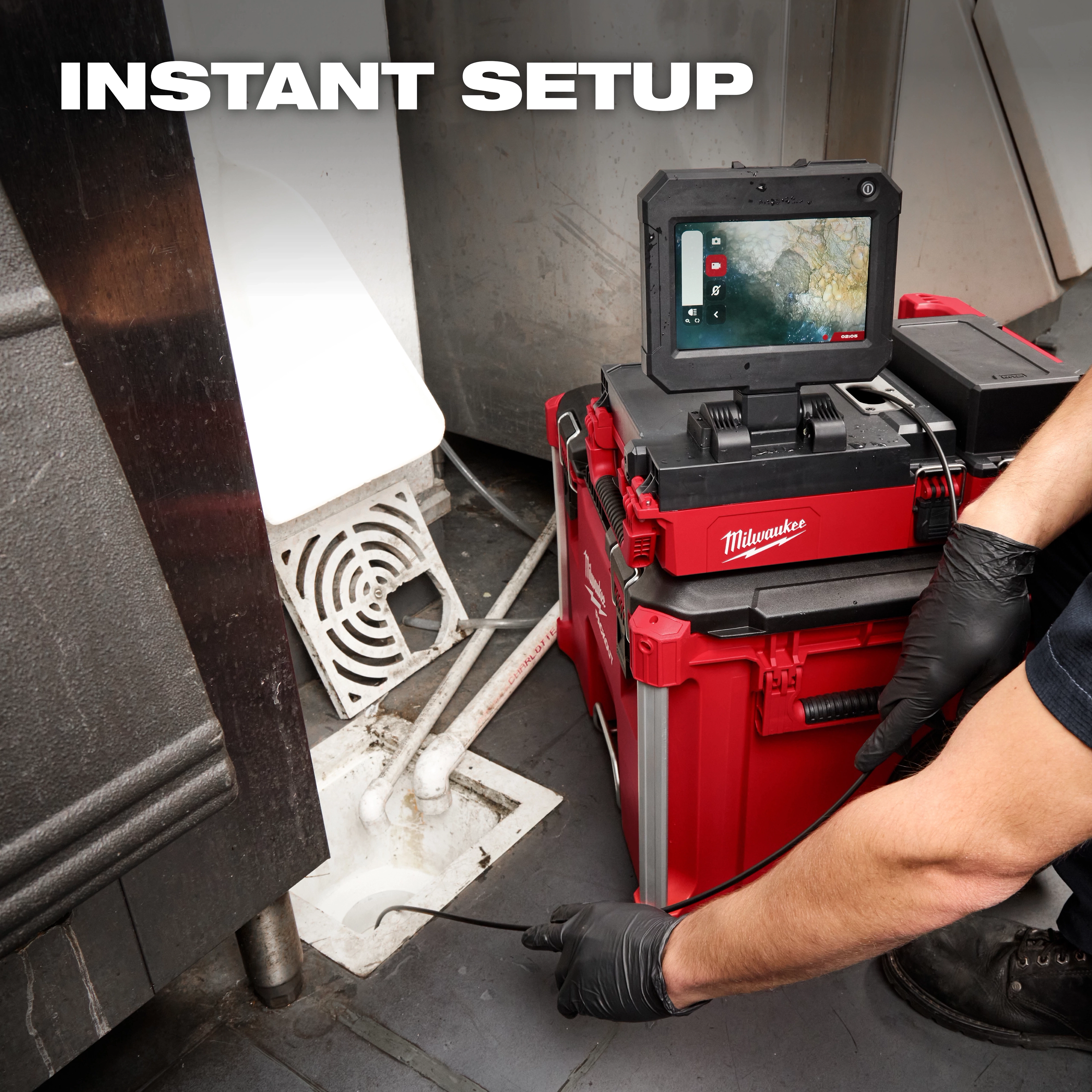 A person uses the M12™ 75' Drain Camera with PACKOUT™ Compatibility to inspect a drain. The camera system is displayed on a red portable unit with a screen showing the pipe interior. Text reads "INSTANT SETUP."