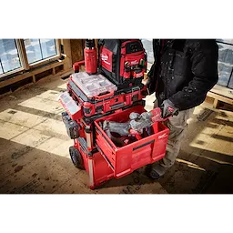 Milwaukee Packout rolling toolbox stacked with red tool cases and bags on a construction floor.