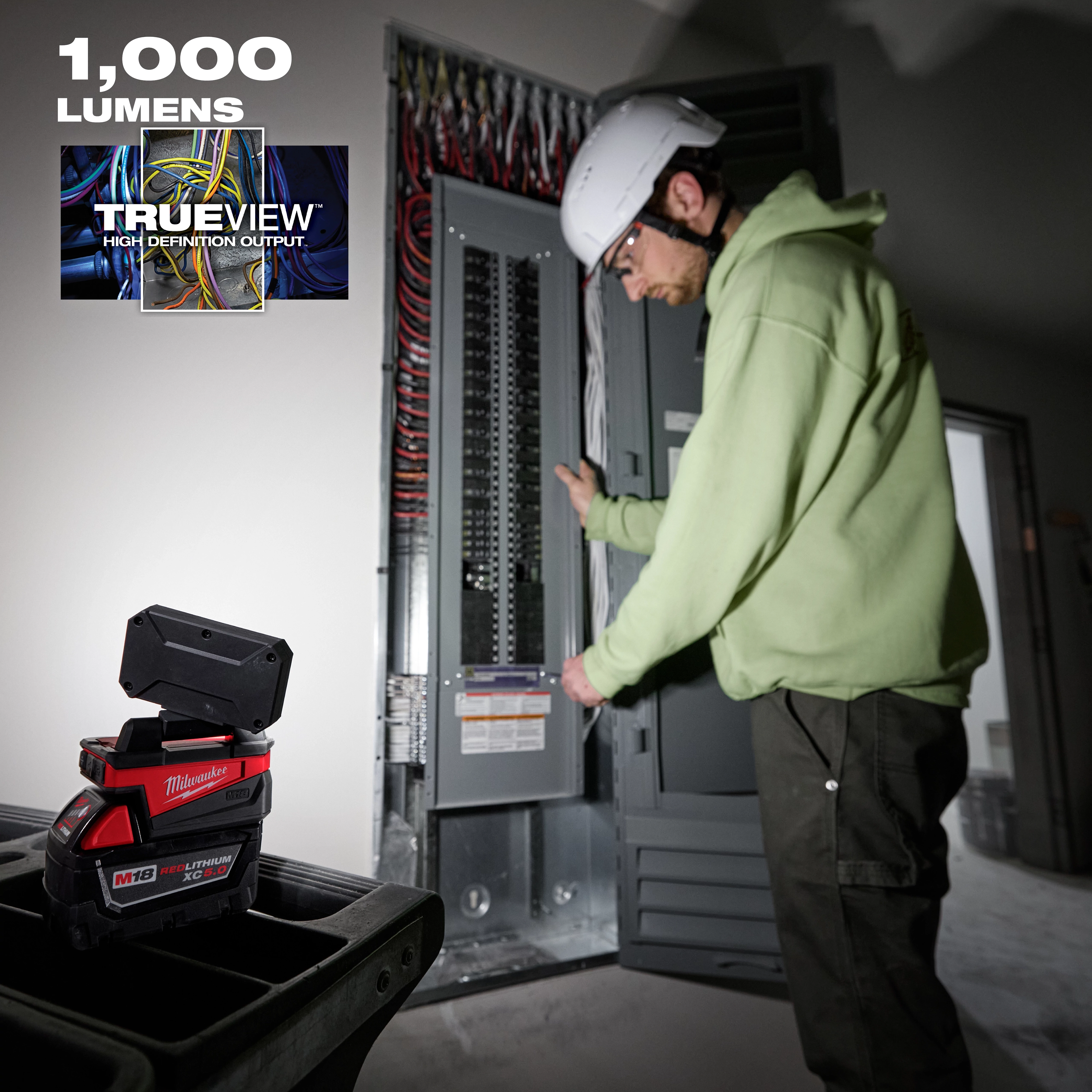 Person wearing a hard hat working with an electrical panel, illuminated by a Milwaukee TRUEVIEW light displaying "1,000 lumens."