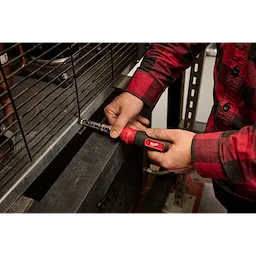 Person in a red plaid shirt using a 7-IN-1 HOLLOWCORE Multi-Nut Driver to tighten a bolt on a metal structure.