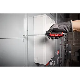 Gloved hand using 3/8" Slotted 8" Cushion Grip Screwdriver (USA) to turn a screw on a metal electrical panel.