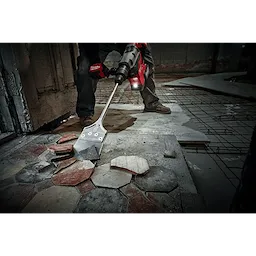 Worker using the SDS MAX Floor Scraper to remove old tiles from a concrete floor in a construction or renovation site.