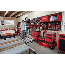 A man organizes tools on PACKOUT Large Wall Plate units in a workshop, surrounded by red storage boxes and woodworking equipment.