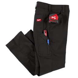 A pair of black work pants with multiple pockets. The pants have a Milwaukee 25-foot measuring tape, a red tool, and a blue pen visibly tucked into the pockets. There is a Milwaukee logo patch on one of the pockets.