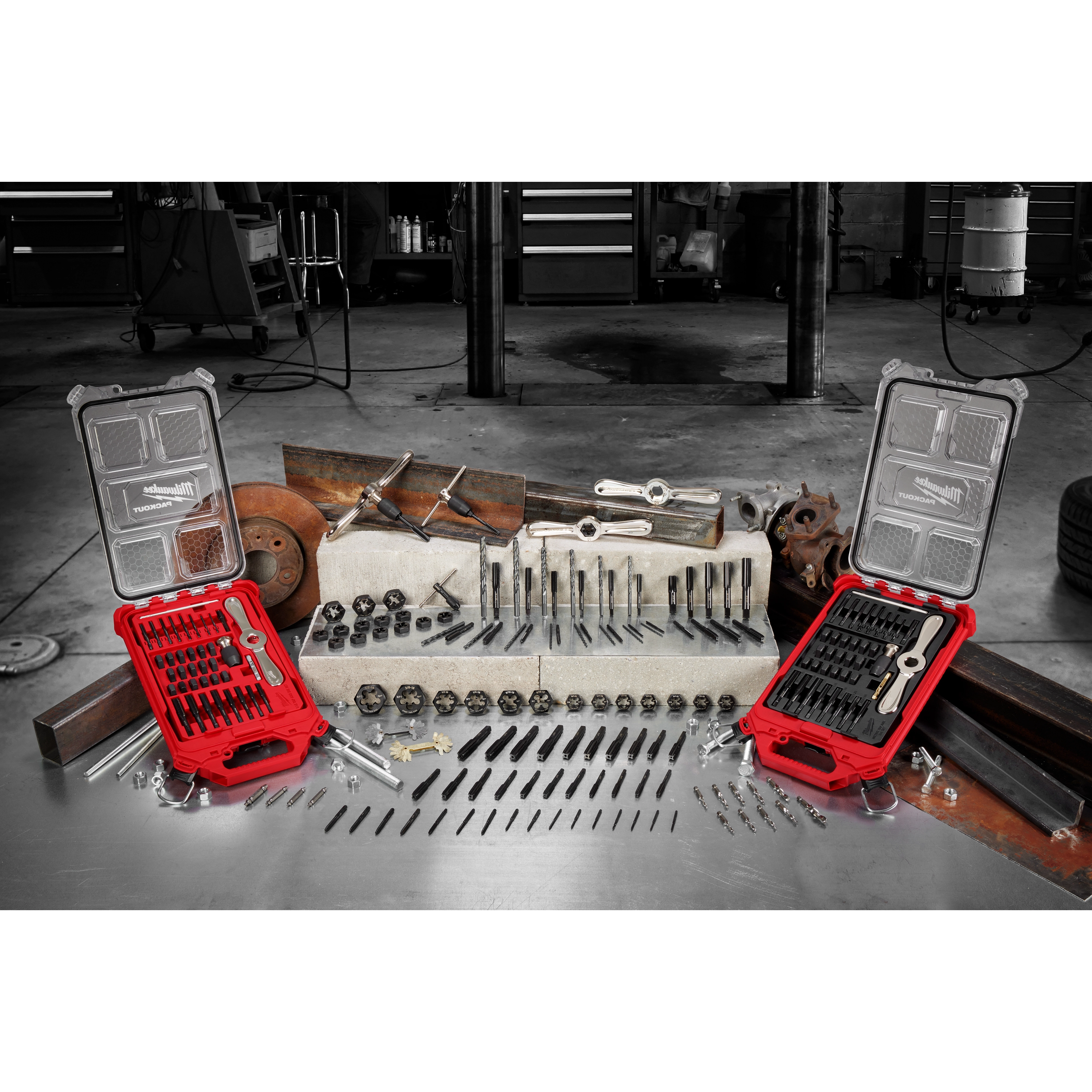 The March 2023 Taps and Dies Family product displays various taps and dies laid out on a workbench, accompanied by two red carrying cases. Behind it are workshop tools and machinery. Items include drill bits, screw extractors, tap wrenches, and dies, organized to show different sizes and uses.